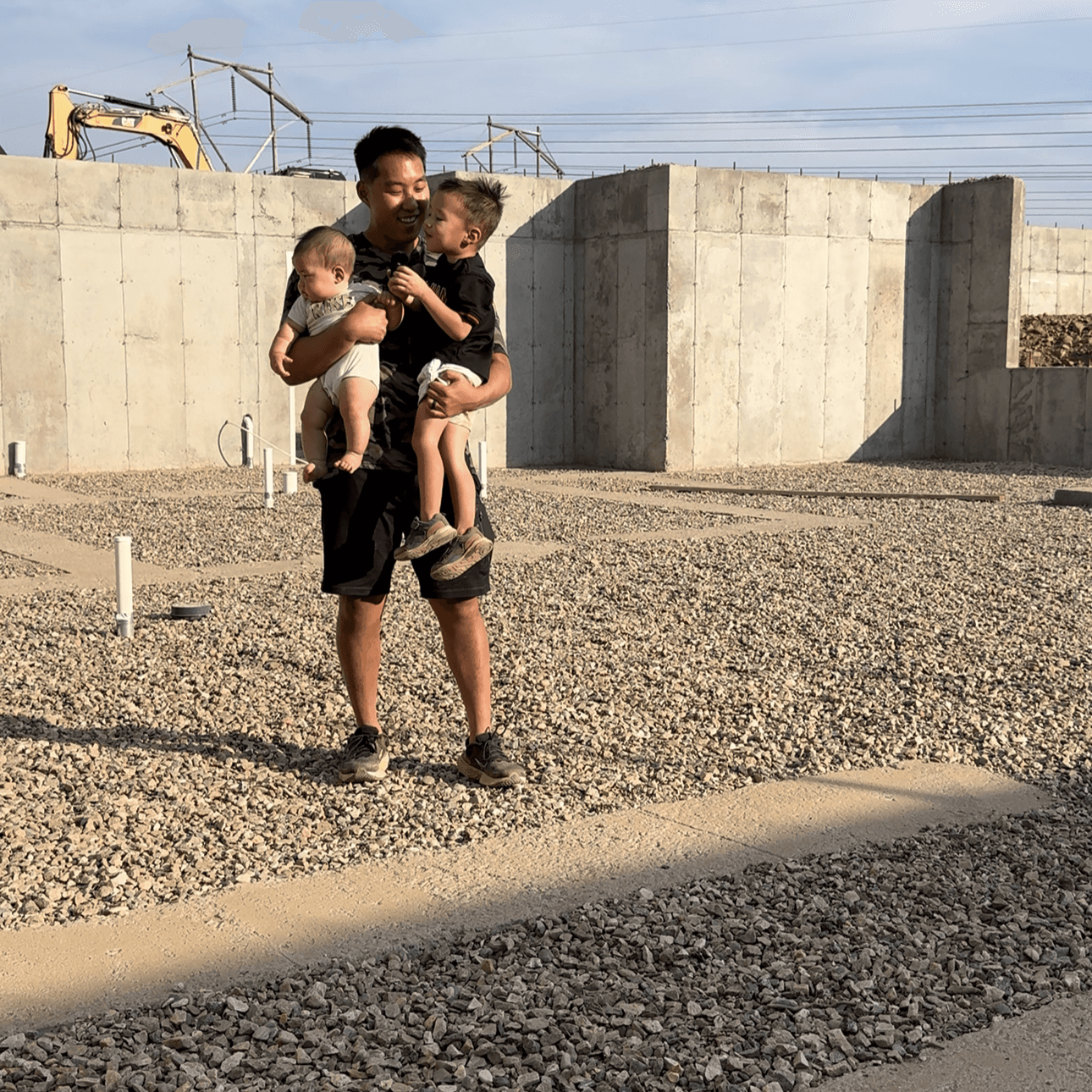 Preston Seo carrying his two children across the concrete foundations of a build in progress